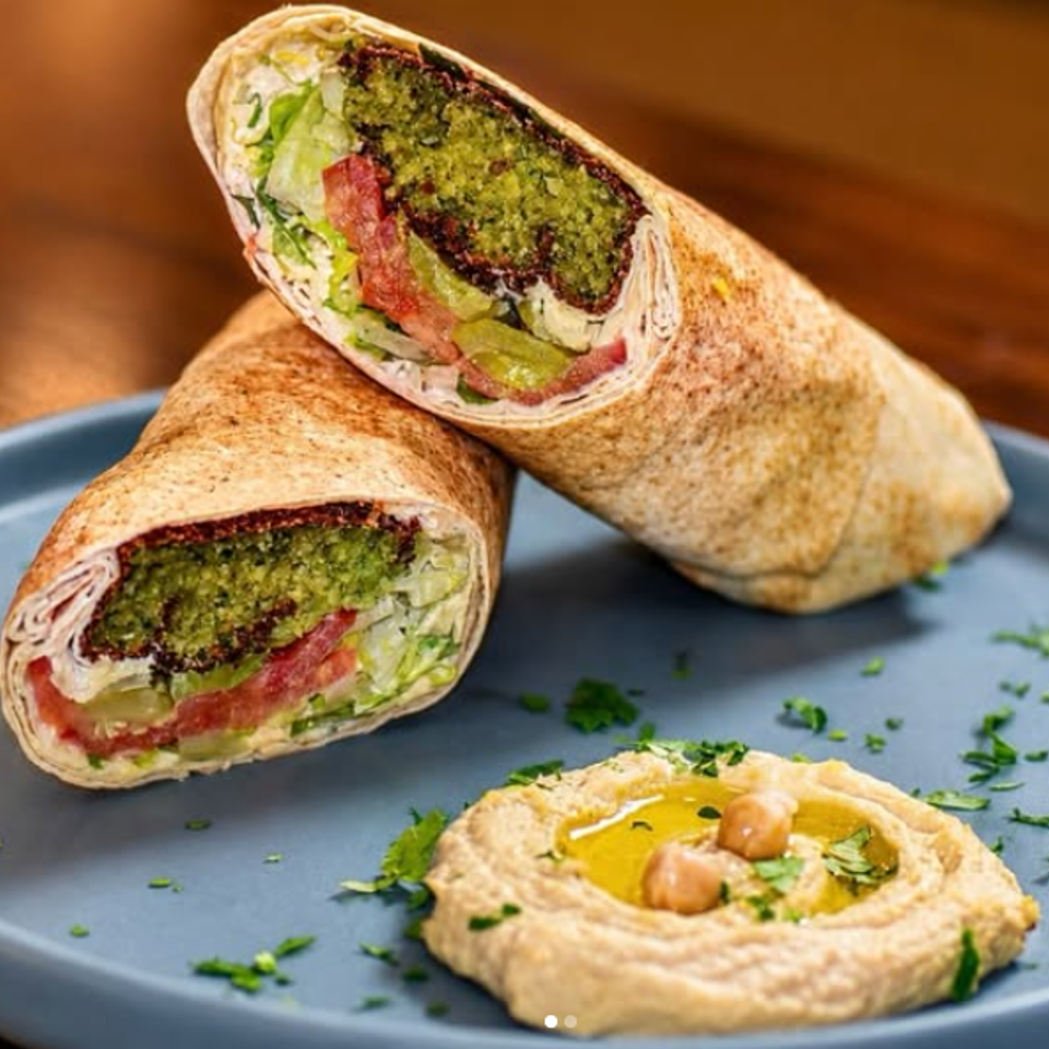 Two sliced falafel wraps with vegetables and hummus garnished with herbs on a blue plate.